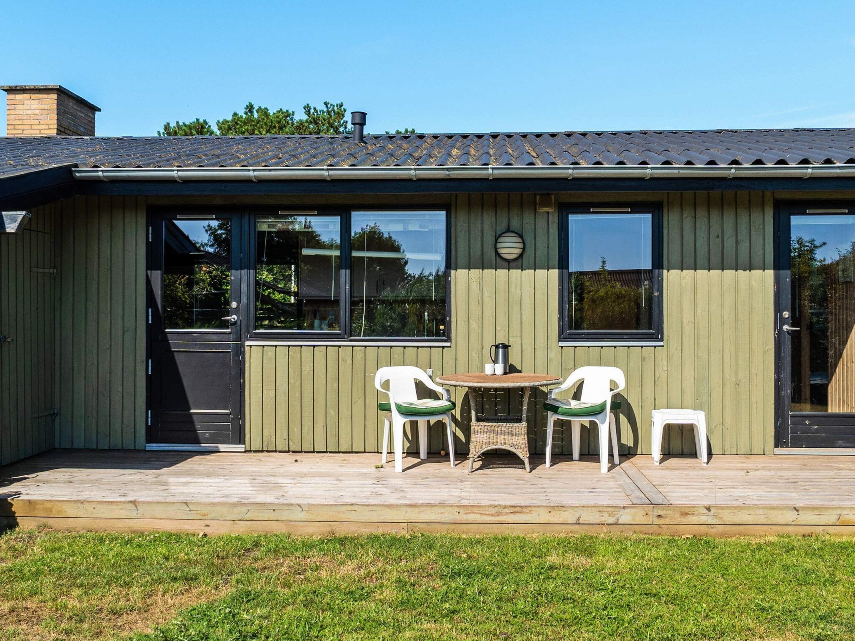A wooden building with a deck, two white chairs, a table, and a window.