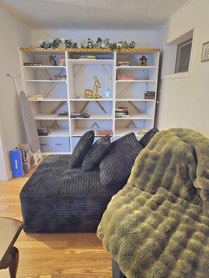 Ein Zimmer mit einer Eckcouch, einem Bücherregal und einem kleinen Tisch.