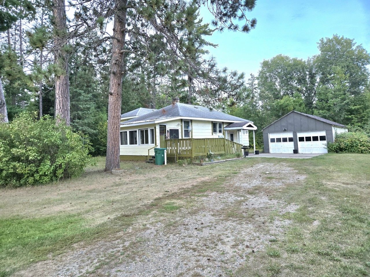 Une propriété résidentielle comprenant une maison et un garage, entourée d’arbres et dotée d’une cour gazonnée.