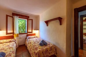 Una habitación con dos camas, una ventana con cortinas, una estantería de madera y piso de baldosas.