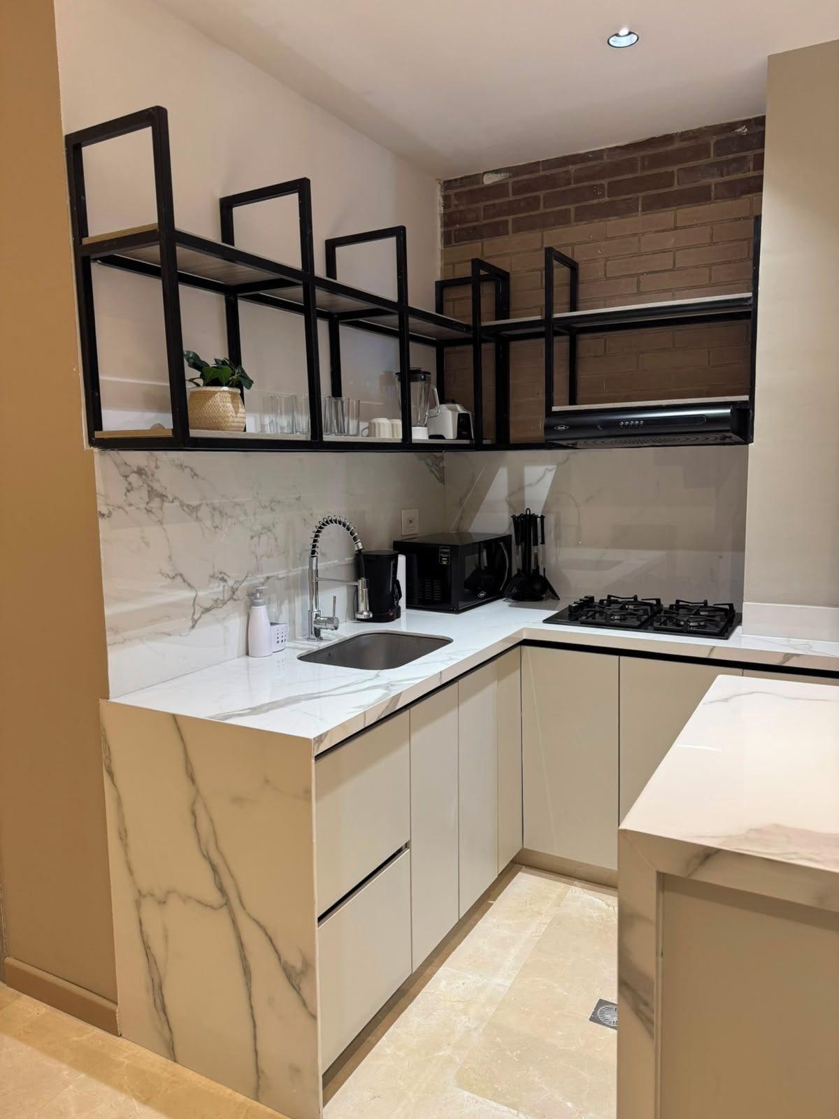 A modern kitchen with marble countertops, a built-in stove, and black shelving units.
