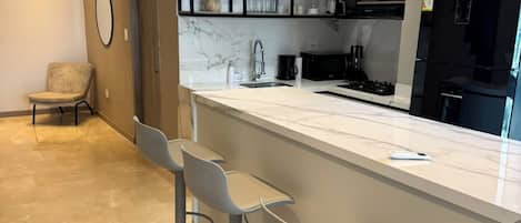 A modern kitchen with a marble countertop, black appliances, and a bar area with stools.