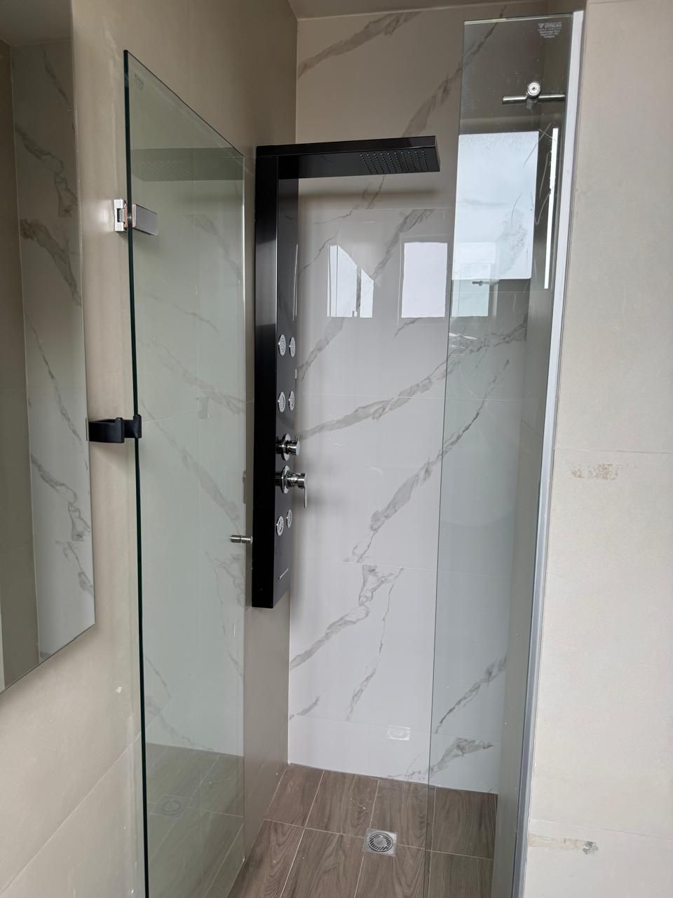 Un baño moderno con cabina de ducha de vidrio, paredes de mármol y suelo de madera.