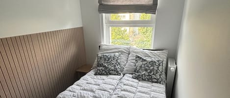 A bedroom with a bed, a window with blinds, and a radiator.
