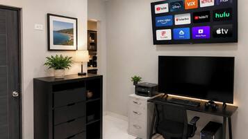 Un bureau moderne, aménagé dans une maison, avec un grand téléviseur à écran plat diffusant divers services de streaming, un ordinateur de bureau et un fauteuil de bureau confortable.