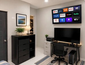 A modern home office with a large flat-screen TV displaying various streaming services, a desktop computer, and a comfortable office chair.