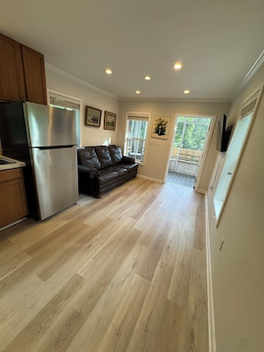 A kitchen with a stainless steel refrigerator, a brown leather sofa, and a wooden floor.