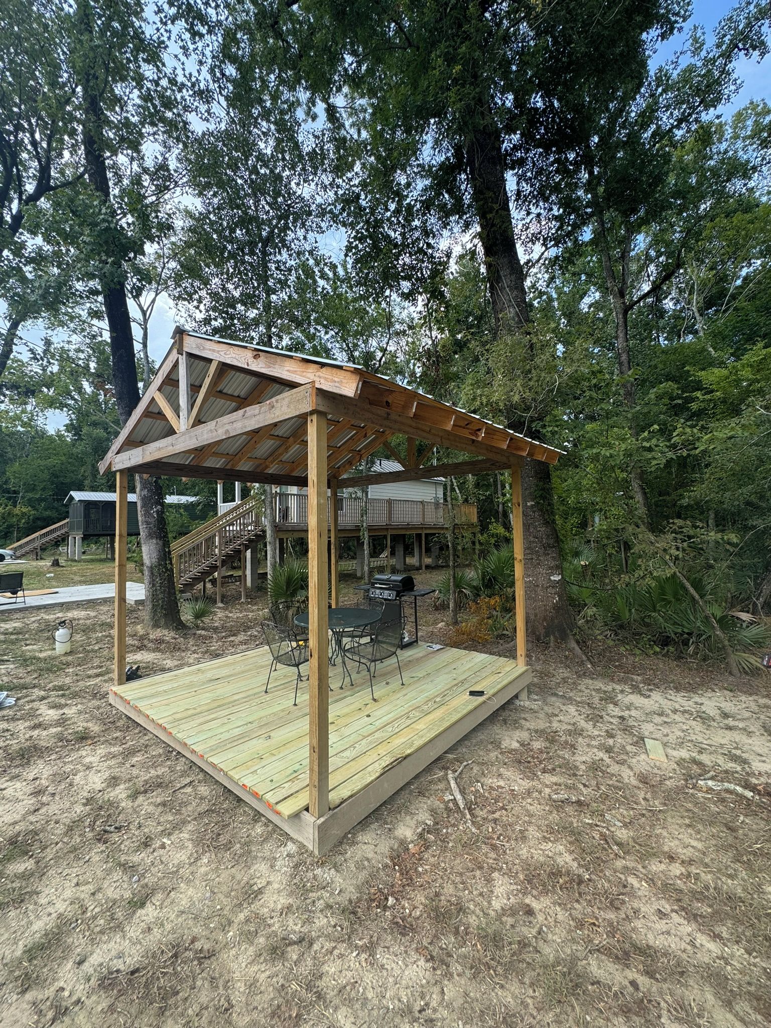 Una estructura de pergola de fusta amb taula i cadires al davall.
