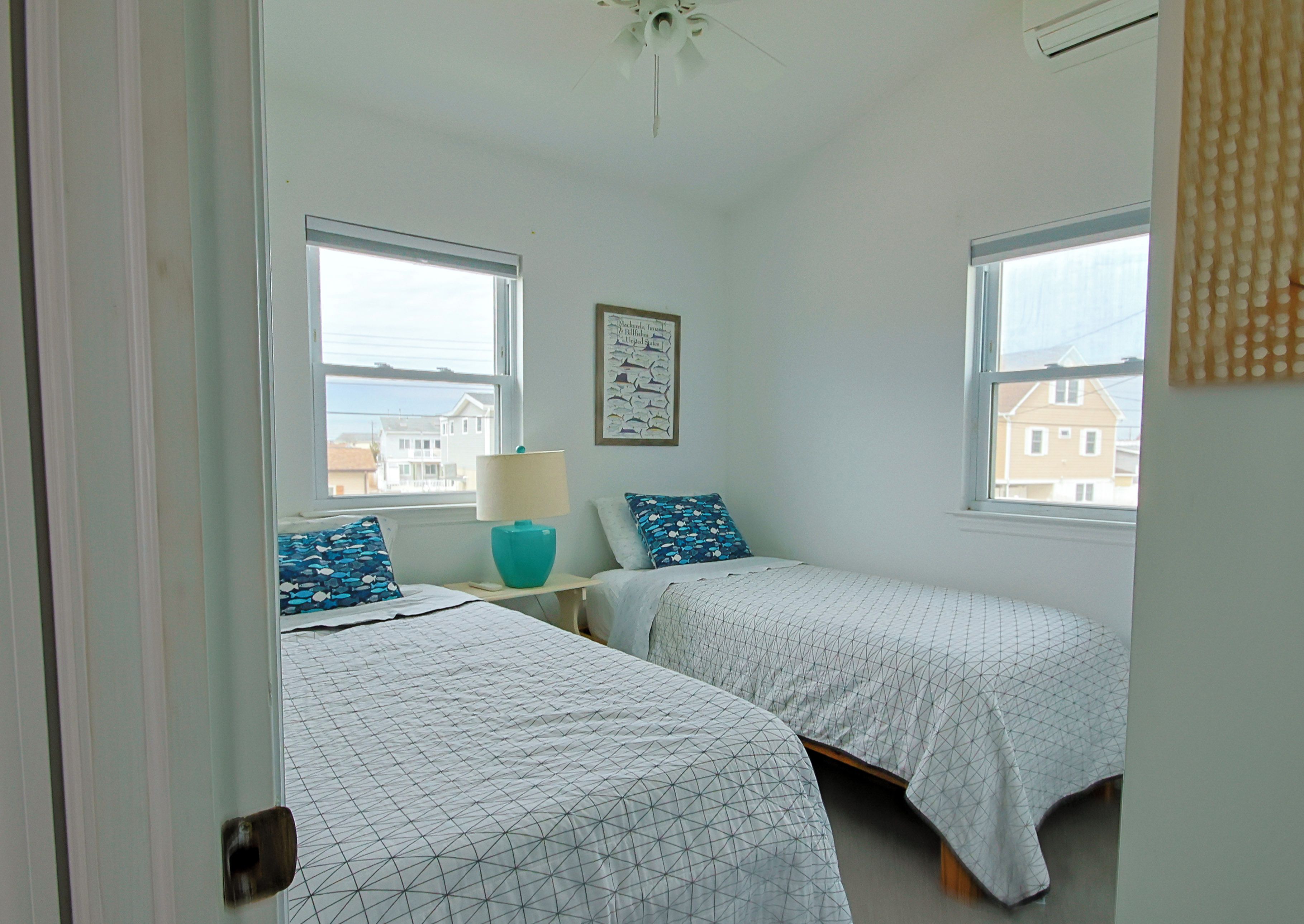 Une chambre avec deux lits simples, un ventilateur de plafond et une fenêtre donnant sur des immeubles.
