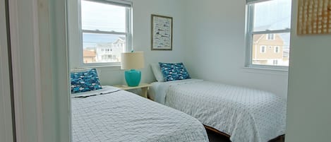Une chambre avec deux lits simples, un ventilateur de plafond et une fenêtre donnant sur des immeubles.