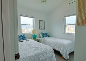 A bedroom with two single beds, a ceiling fan, and a window with a view of buildings. - Cozy 2-bedroom house on beautiful lagoon (Stafford Township)