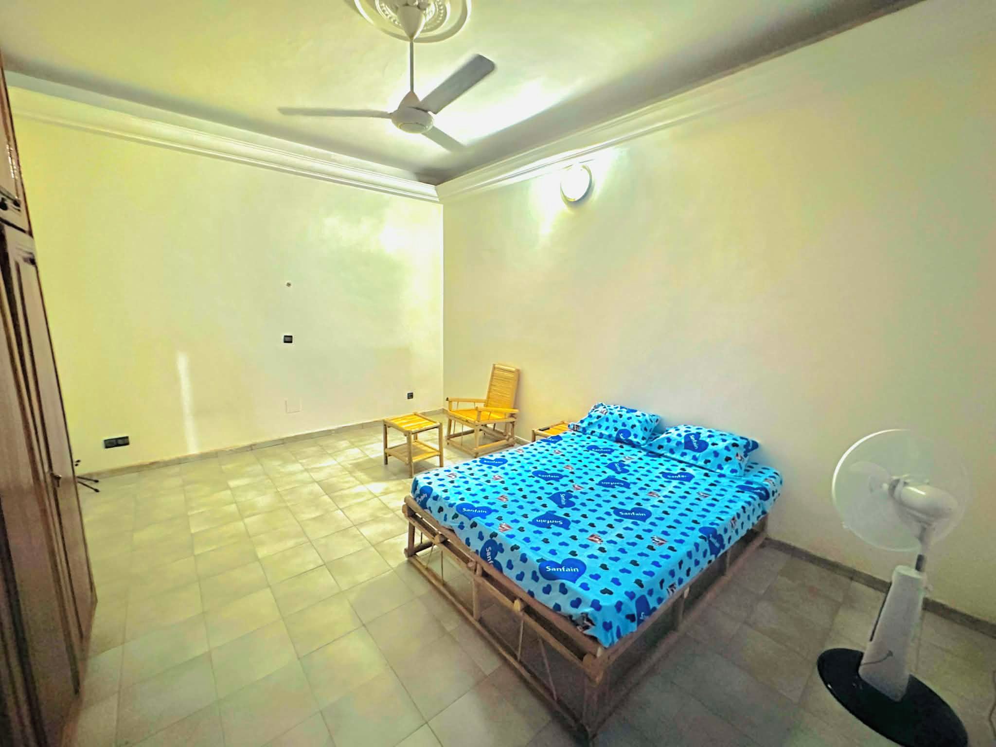 Een kamer met een bed, een stoel, een ventilator en een plafondventilator.
