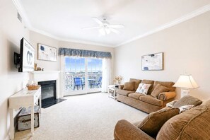 A living room with a fireplace, a sofa, a television, and a ceiling fan. - Laguna Vista 304 (Ocean City)