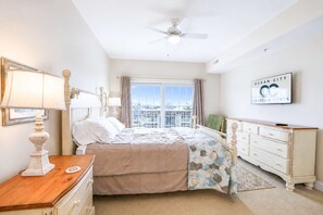 Ein Schlafzimmer mit Bett, Kommode, Nachttisch, Lampe und Blick auf die Stadt durch das Fenster.