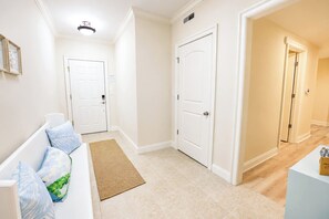 A hallway with a white bench, two white doors, a light switch, and a ceiling light fixture. - Laguna Vista 304 (Ocean City)