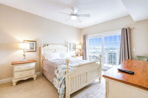 A bedroom with a bed, bedside tables, a ceiling fan, a window with curtains, and a view of buildings. - Laguna Vista 304 (Ocean City)