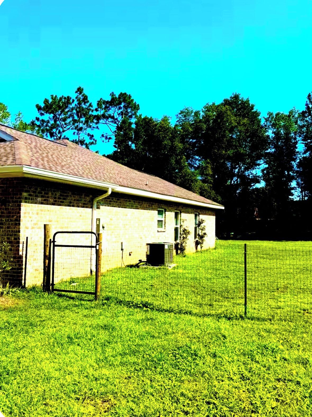 A single-story brick building with a covered porch, a fenced yard, and trees in the background.