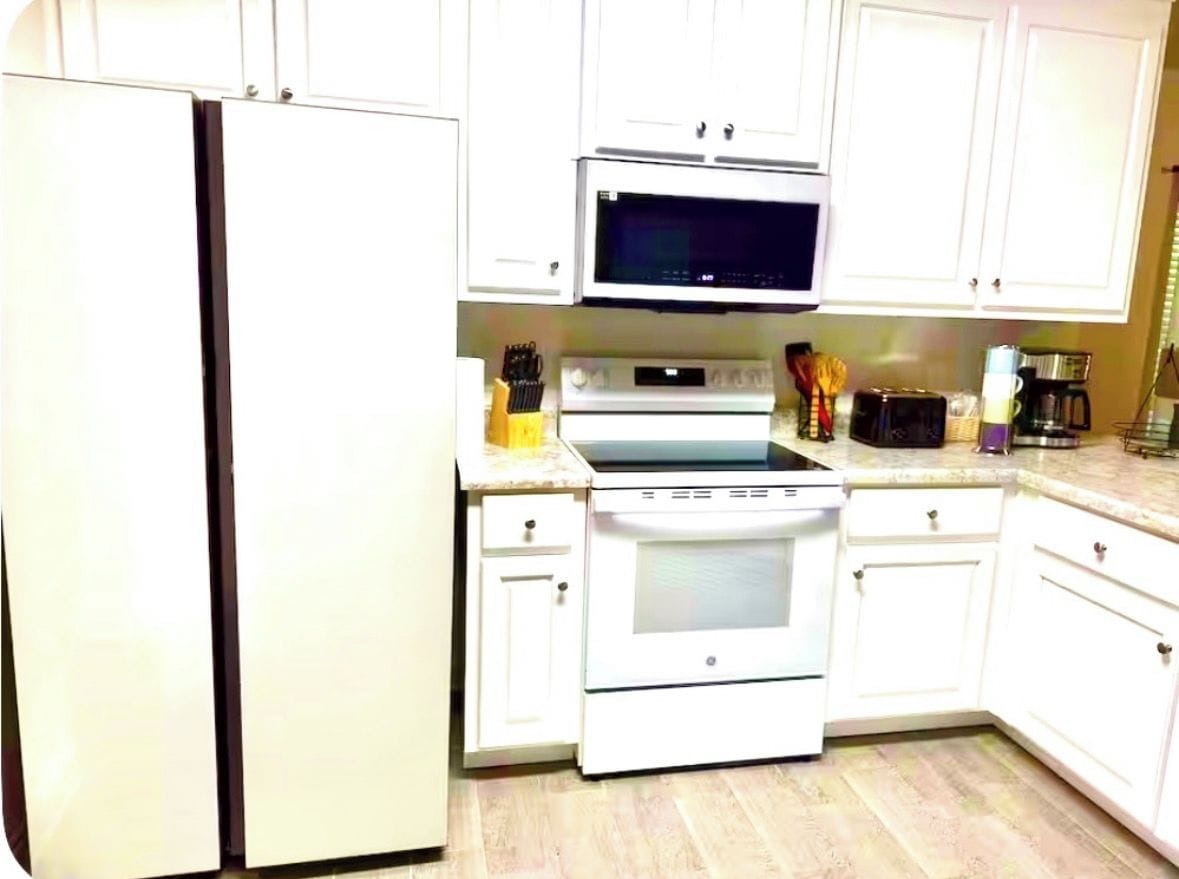A kitchen with white cabinets, a refrigerator, a microwave, an oven, and a coffee maker.