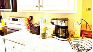 A kitchen with white cabinets, a stove, a coffee maker, and a microwave.