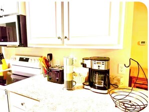 A kitchen with white cabinets, a stove, a coffee maker, and a microwave.