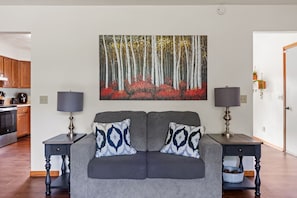 A living room with a grey sofa, two matching side tables, and a painting of a forest. - Family Home Near Dells Waterparks | Papas' Legacy (Wisconsin Dells)