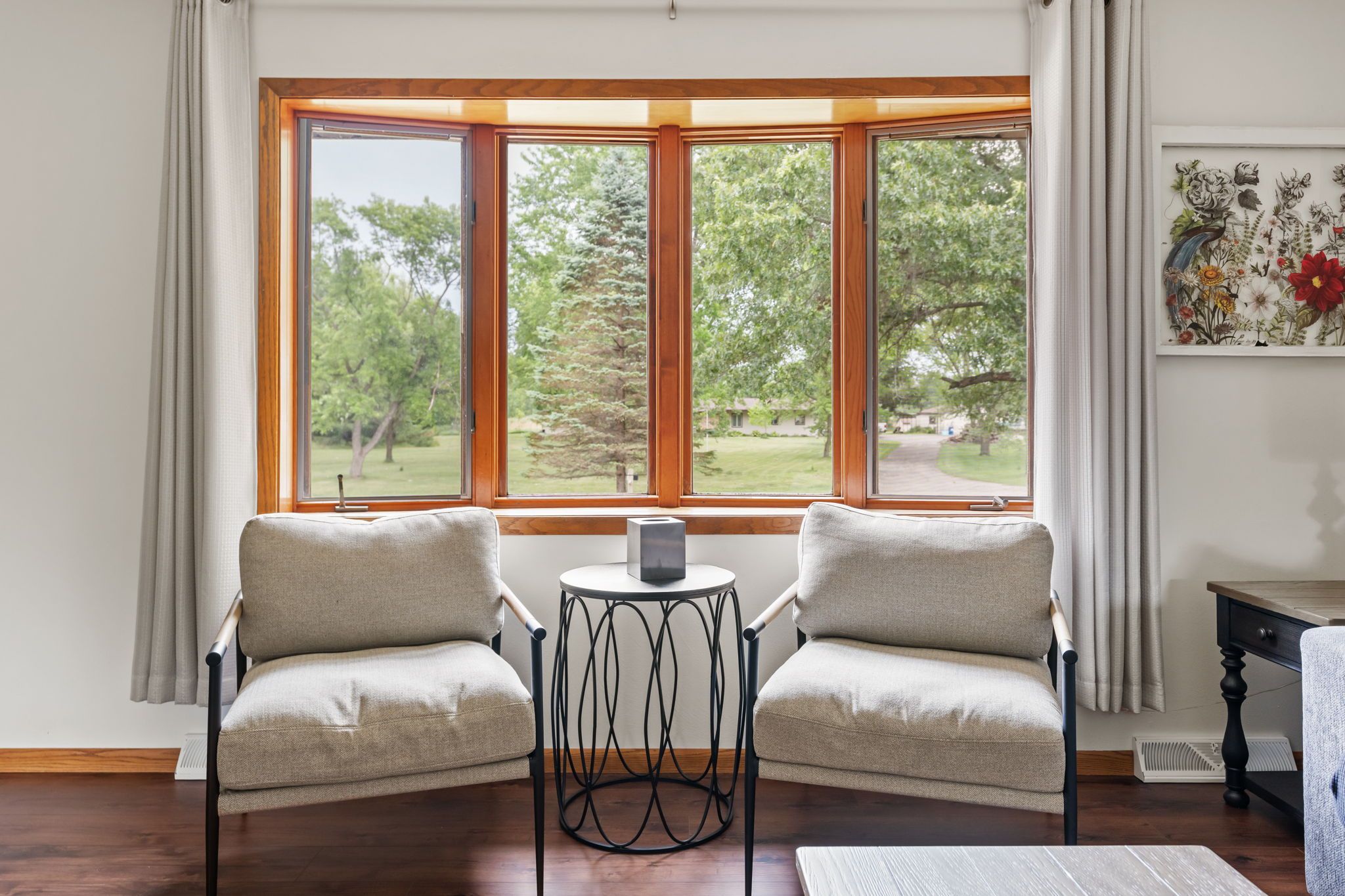 A room with two armchairs facing a large window with a view of trees and a lawn.