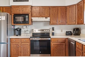 A kitchen with wooden cabinets, a microwave, a stove, and a coffee maker. - Family Home Near Dells Waterparks | Papas' Legacy (Wisconsin Dells)