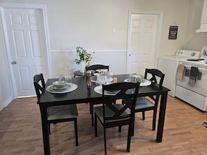 A dining area with a table set for four, chairs, a small plant, and a white appliance in the background.