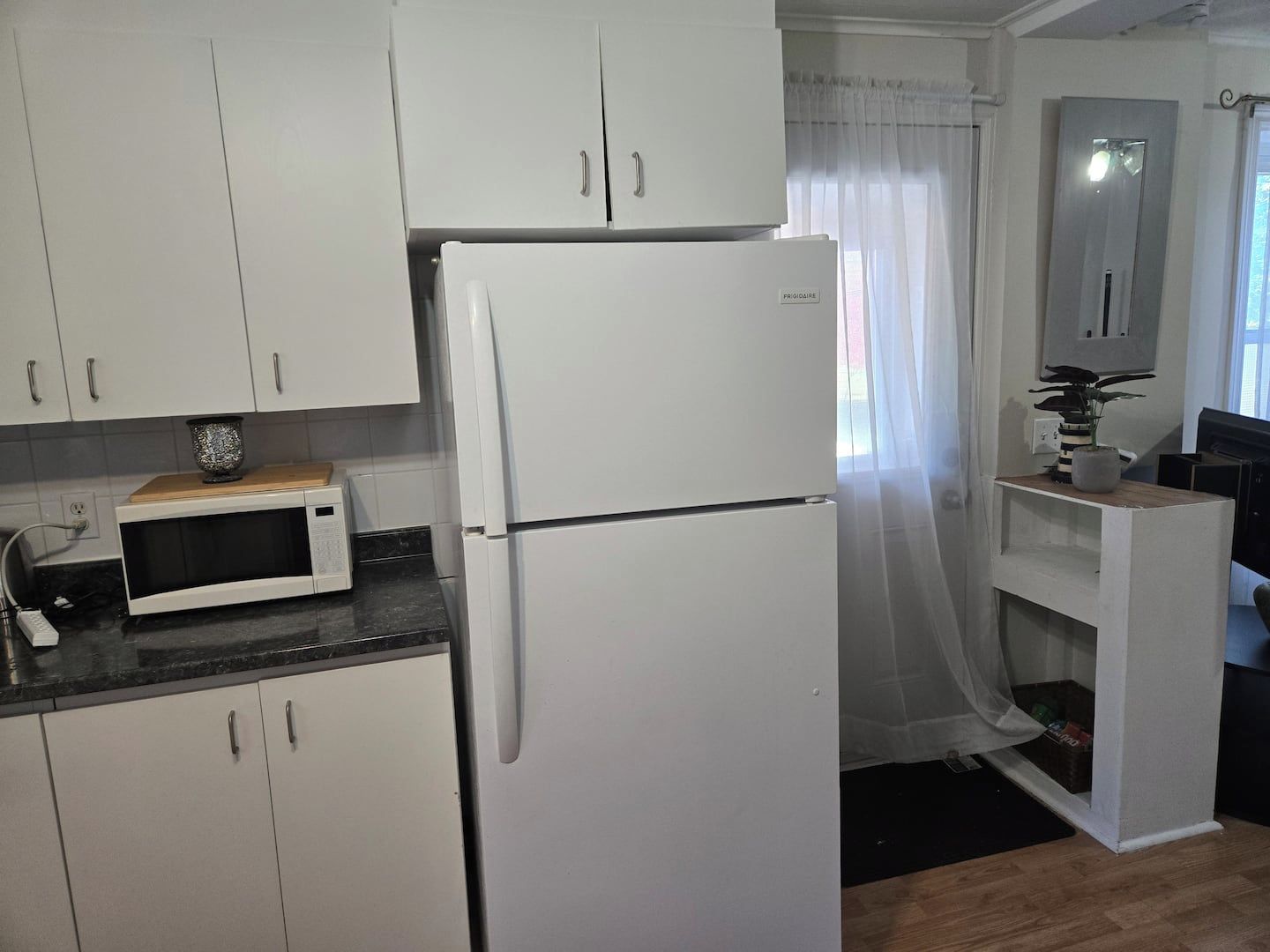 Una cucina con mobili bianchi, un frigorifero bianco, un forno a microonde e un piccolo bancone in legno.