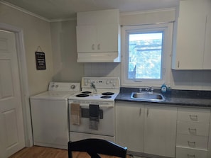 A compact kitchen with white cabinets, a stove, and a window.