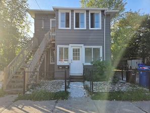 A two-story residential building with a front door, a staircase, and a fenced yard. - Quiet 2-bedroom near Ottawa – Wi-Fi and free parking (Gatineau)