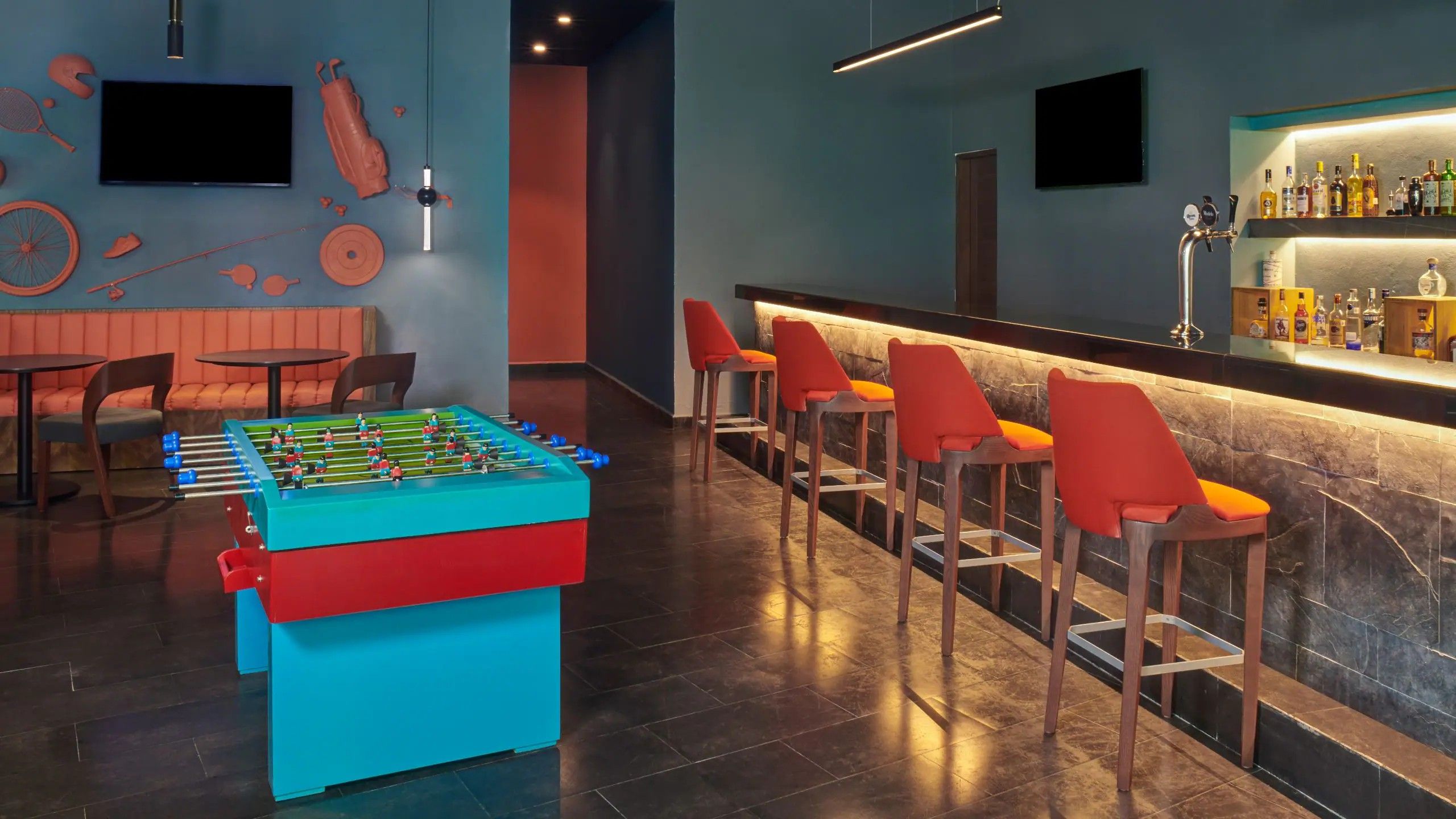 Zona de bar con una mesa de fútbol, taburetes y una barra con botellas.