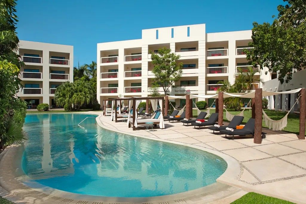 Una piscina con sillones de descanso y un edificio con balcones al fondo.