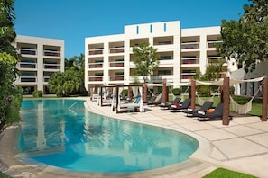 Una piscina con sillones de descanso y un edificio con balcones al fondo.