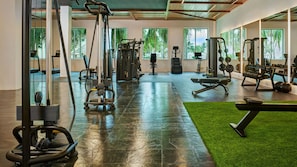 Un gimnasio con diverso equipo de ejercicio, amplias ventanas y una zona de césped artificial verde.