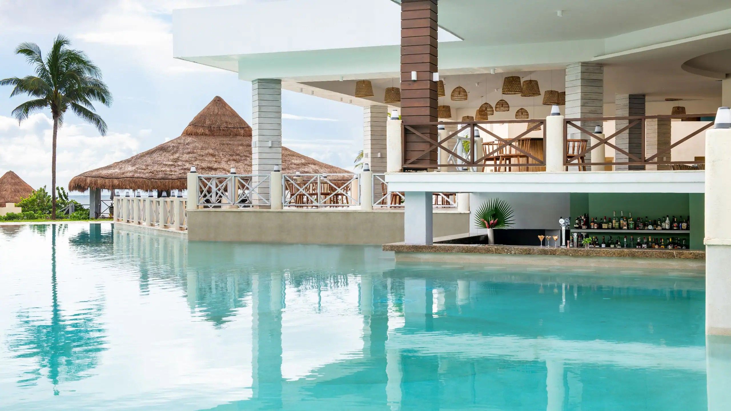 Una piscina di un resort con area bar, palme e strutture a tetto di paglia.