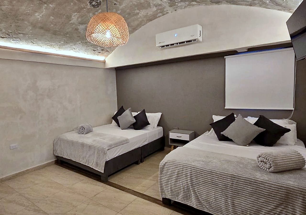 A modern bedroom with two beds, a ceiling light, and a wall-mounted air conditioner.