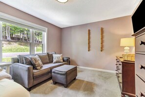 A living room with a sofa, ottoman, and a lamp on a dresser. - Upscale Winterplace 3BR | Steps to Ski Access (Ludlow)