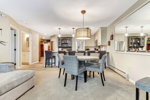 A modern kitchen with a dining area, featuring a round table with patterned chairs, pendant lighting, and built-in cabinets. - Upscale Winterplace 3BR | Steps to Ski Access (Ludlow)