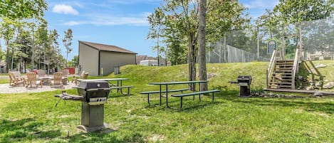 An outdoor area with picnic tables, a barbecue grill, and a building in the background.