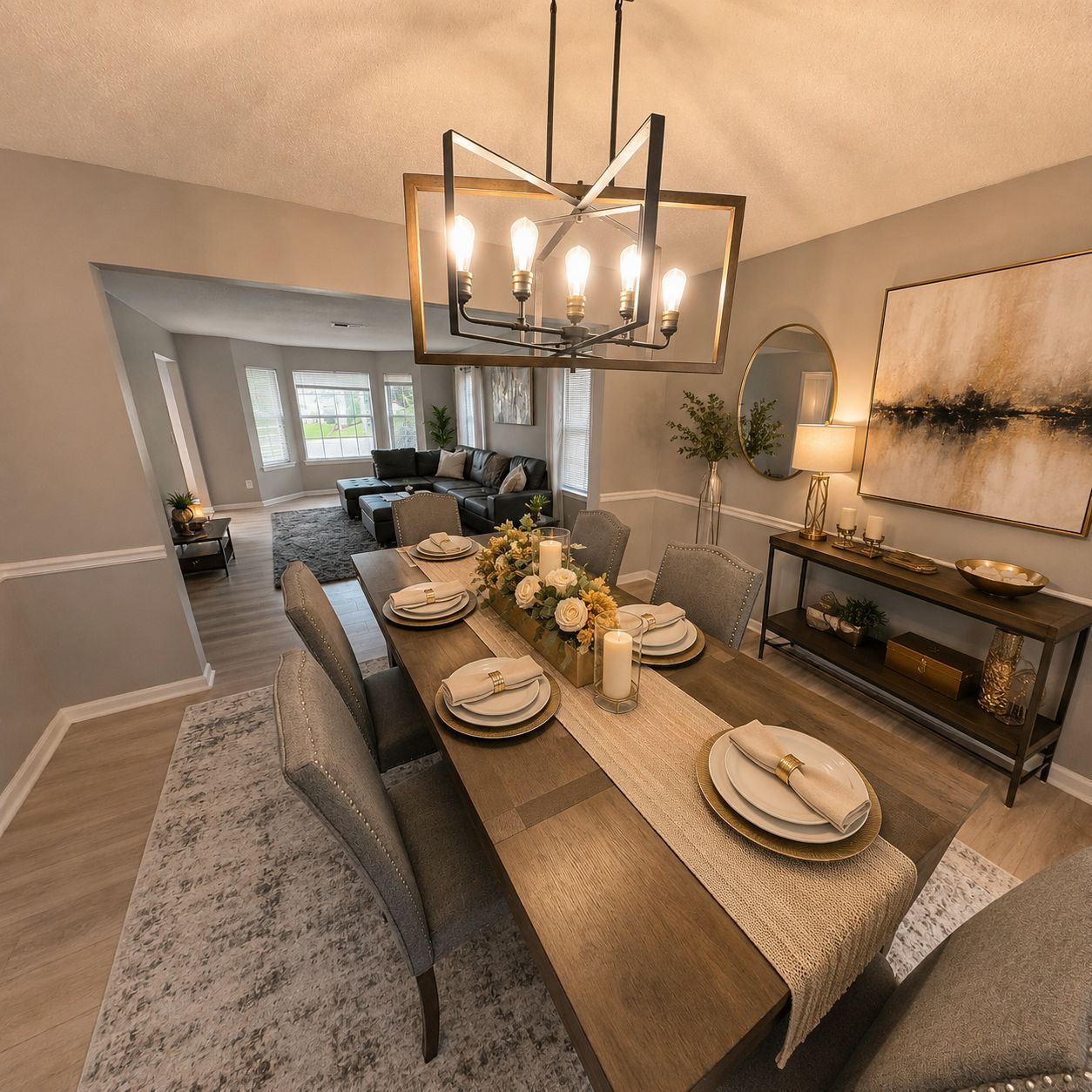 A dining area with a long wooden table set for six, a chandelier, and a large painting on the wall.