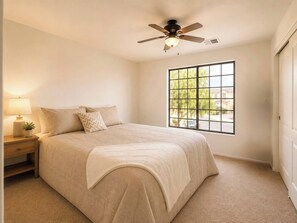 Una camera da letto con un letto, un comodino, una lampada, una finestra e una ventola a soffitto.