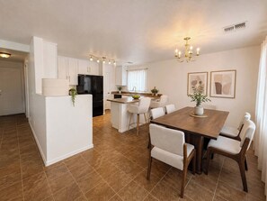 Una cucina moderna con mobili bianchi, un frigorifero nero e un'area pranzo con tavolo e sedie in legno.