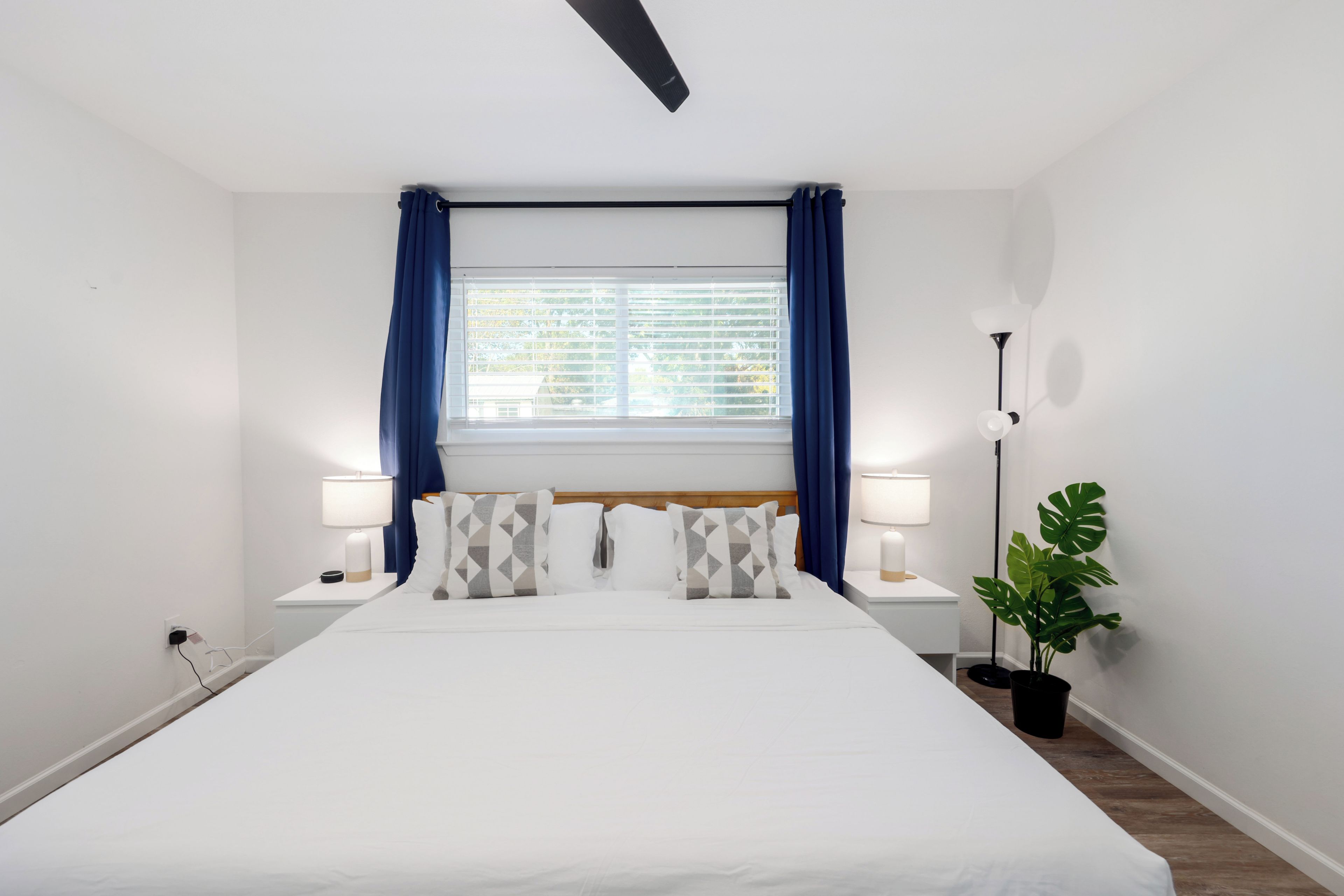 Een hotelkamer met een groot bed, twee nachtkastjes met lampen, een raam met gordijnen en een potplant.