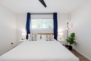 A hotel room with a large bed, two bedside tables with lamps, a window with curtains, and a potted plant. - 3BR Retreat in Austin — Massage chair & Firepit (Austin)