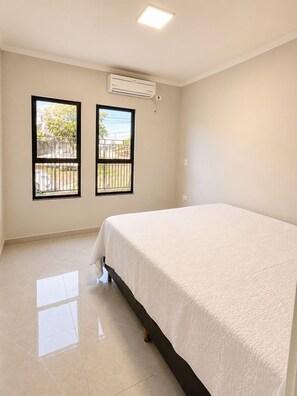 A room with a bed, two windows, an air conditioning unit, and a tiled floor.