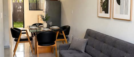 Una sala de estar moderna con un sofá gris, un comedor con mesa y sillas, y dos obras de arte enmarcadas en la pared.