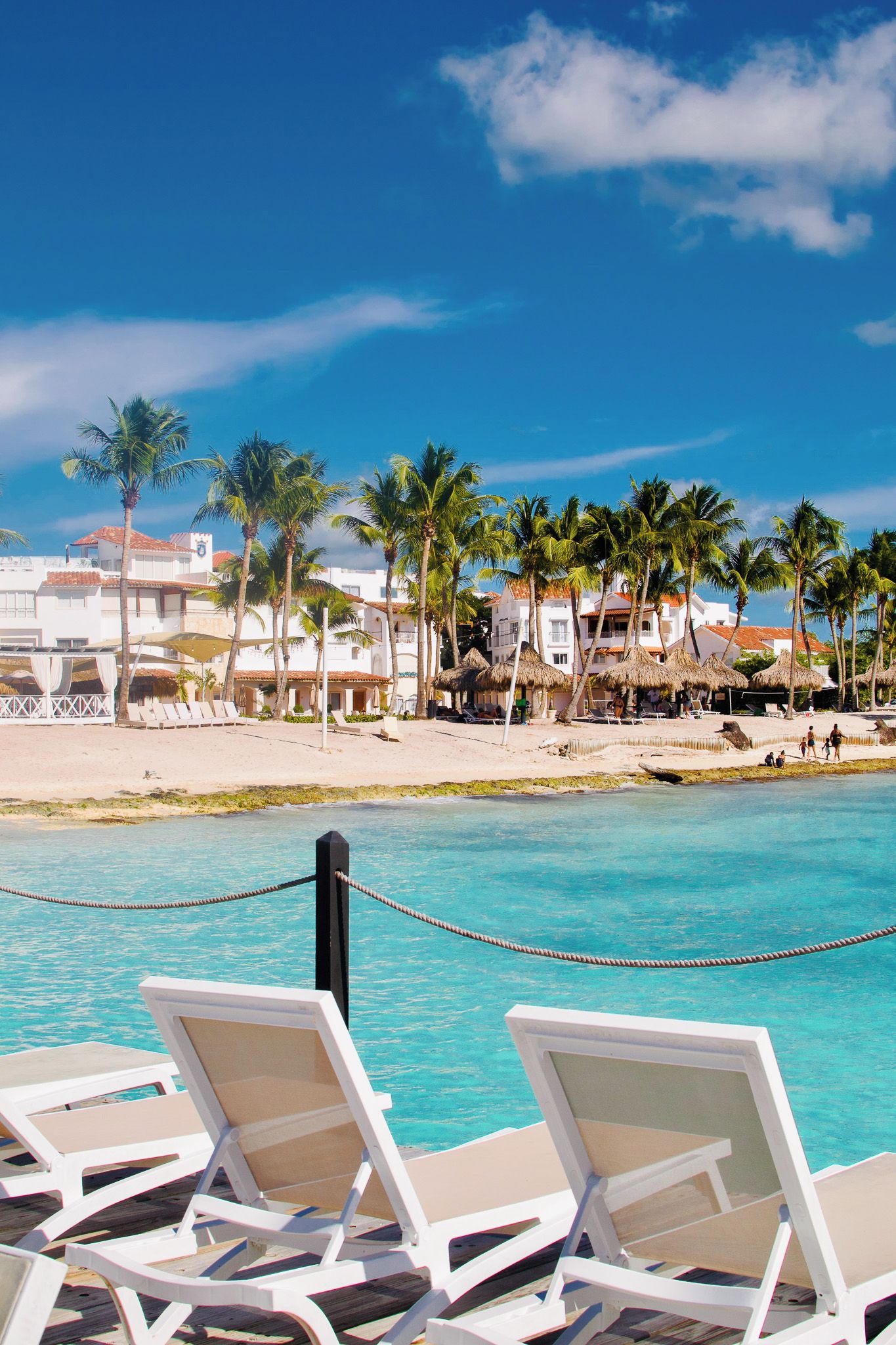 A beachfront hotel with white buildings, palm trees, and a clear blue sky.