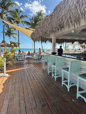 A wooden deck with outdoor seating, a bar area, and a view of the beach and ocean. - Flamenco Studio in Cadaques Caribe (San Rafael del Yuma)