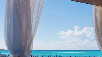 Vista a la playa con una terraza de madera y cortinas blancas.